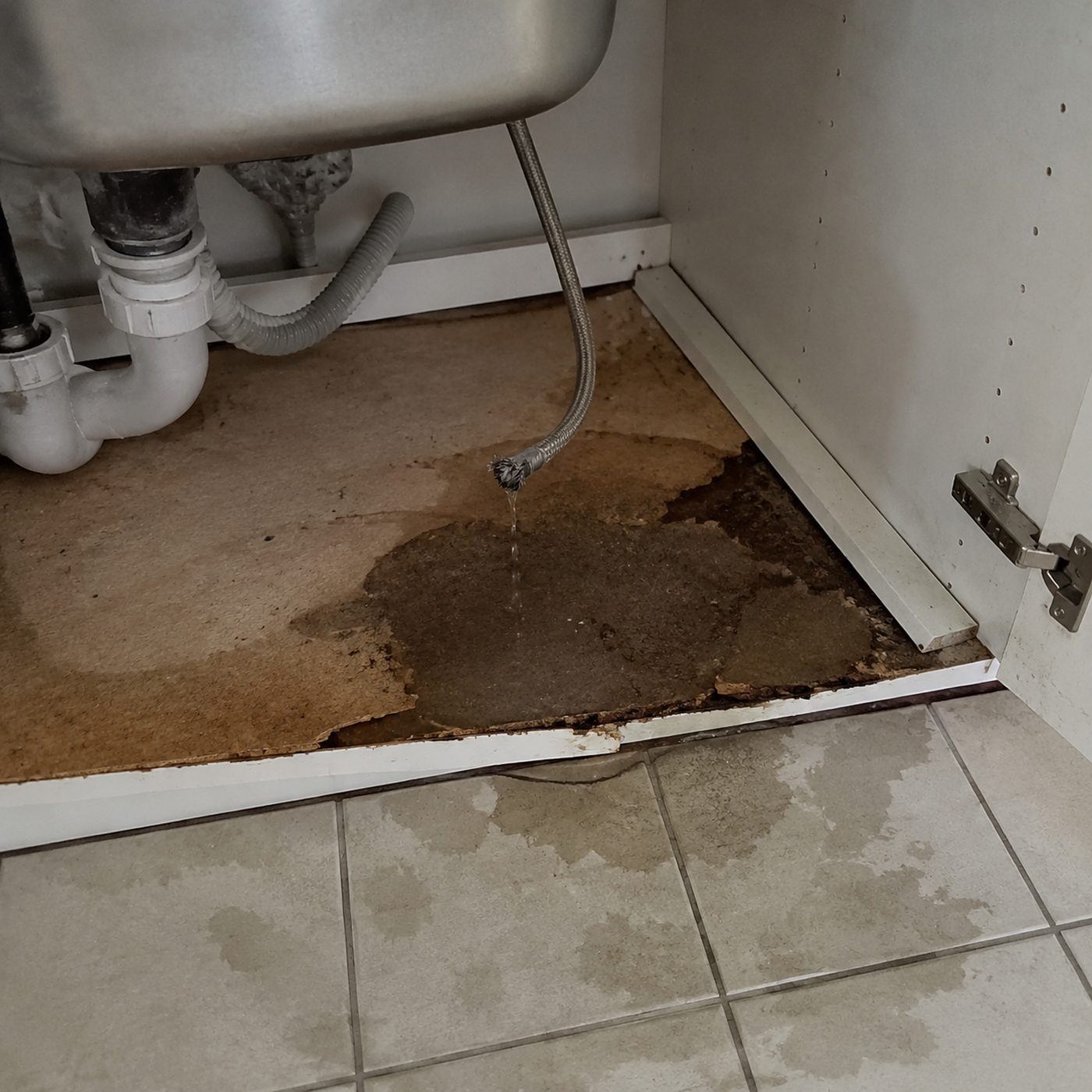 A burst flexible hose leaking under a kitchen sink